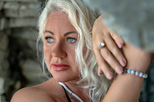 Blue eyed blonde woman wearing beaded jewelry looks away in a thoughtful portrait