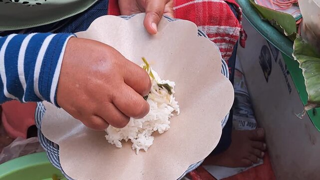 Street food vendor preparing Blitar pecel rice with peanut sauce, vegetables, serundeng and fried egg. Traditional Indonesian food, wrapped in paper.