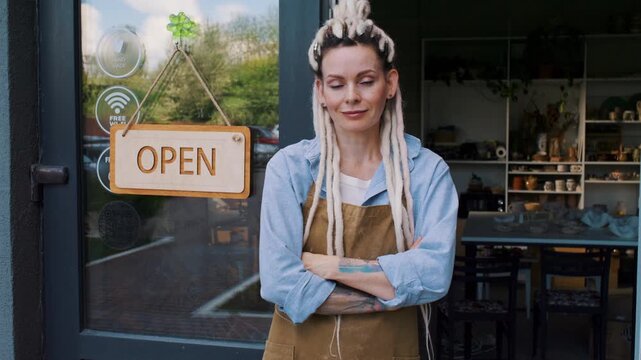 Female potter stands near Open sign at ceramic studio entrance
