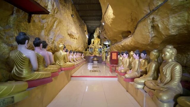 Row of golden buddha statues sitting inside sacred cave temple shrine.