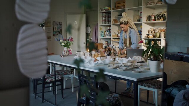 Female potter packs ceramic order at long table in art workshop