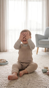 Toddler playing peekaboo with hands covering face in cozy indoor setting  