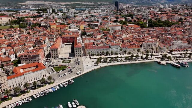 Aerial view of Split waterfront promenade with palm trees, turquoise Adriatic water and old town. Central square with Mediterranean buildings, sunny coastal city.