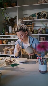 Woman potter smooths ceramic mug surface at worktable in studio