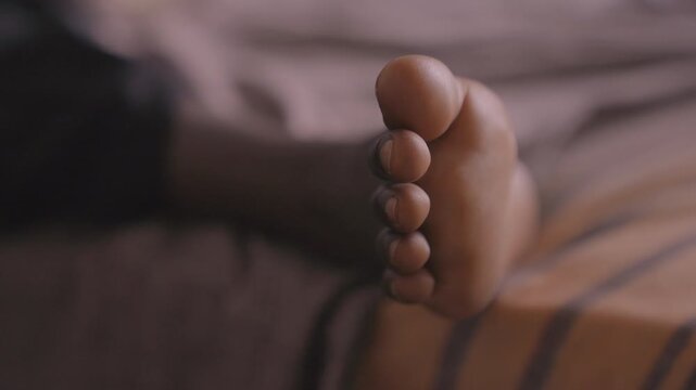 Black daughter toes wiggling on striped mattress, warm evening light, candid closeup, playful tiny foot movement, cozy bedtime routine, soft blanket texture, family warmth, childlike curiosity