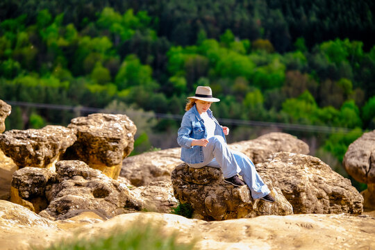 Woman resting on mountain rock in green forest valley. Peaceful summer outdoor recreation and calm travel adventure concept