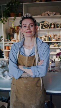 Woman potter stands with crossed arms in creative ceramic studio