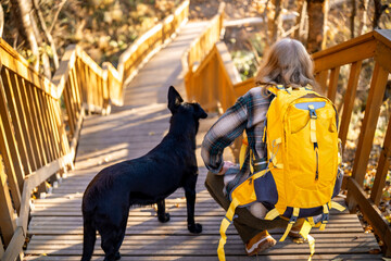 Obraz premium Back view of woman with backpack and black dog resting on wooden stairs
