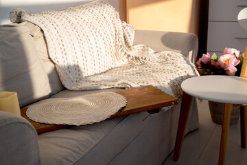 Cozy home interior with beige sofa, knitted blanket, and wooden armrest tray in warm sunlight