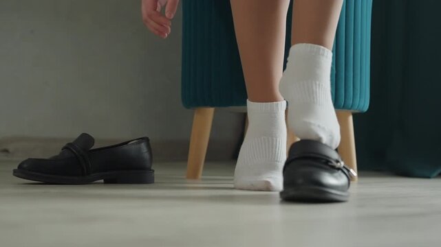 Homebound woman with polished footwear. Indoor scene of woman slipping on loafers before exiting home. Woman in white socks and loafers preparing to head out for work on light floor