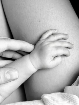 Tender black and white close-up of a newborn baby's tiny hand resting on mother's skin