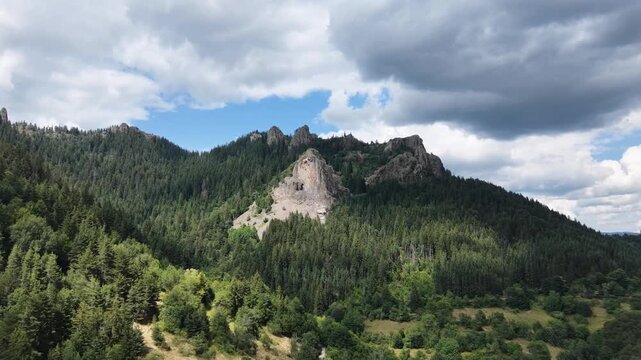 Aerial fly-in shot of a massive rocky cliff and scree slope surrounded by pine forest