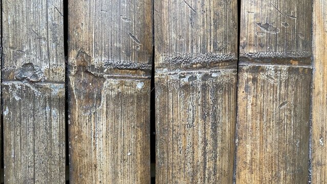 Weathered bamboo panels show natural texture and age. Vertical slats feature deep grooves and faded brown tones. Rustic surface suggests outdoor use or time-worn exposure