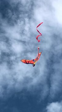 Bright windsurf sail airborne against a dramatic cloudy sky with a trailing safety line. Dynamic outdoor sports scene representing wind power, adventure, motion, and extreme water sports.