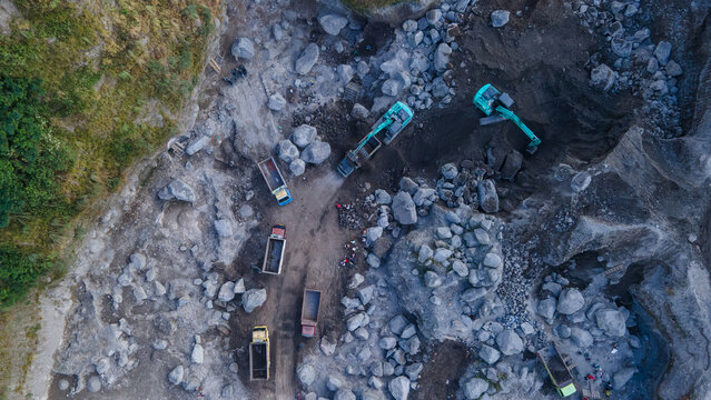 Aerial View of Kaliworo Large-Scale Rock and Sand Quarry with Trucks and Excavators Between Two Steep Forested Cliffs. Active Mining Operation Captured During Morning in Indonesia.