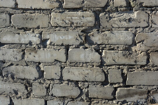 Construction and renovation work, a wall with imperfections and unevenness, the first masonry. A wall of white brick, gray cement, illuminated by the rays of the sun.