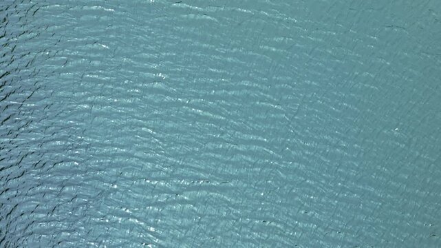 太陽光を受けてキラキラと輝く青い水面、美しい波紋とリフレクションの俯瞰背景

