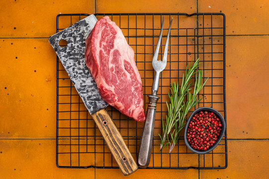 Fresh raw beef chuck eye roll steak on metal rack with butcher tools and herbs. Premium marbled beef meat for cooking.