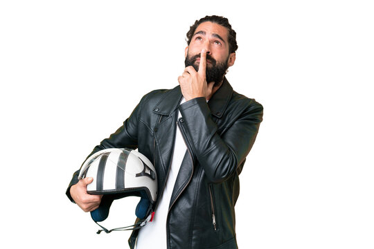 Young man with beard with a motorcycle helmet over isolated chroma key background having doubts while looking up