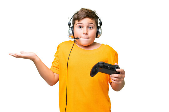 Little caucasian kid playing with a video game controller over isolated chroma key background having doubts while raising hands