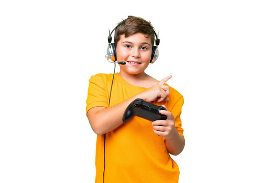 Little caucasian kid playing with a video game controller over isolated chroma key background pointing to the side to present a product