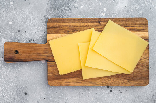 Sliced Gouda style yellow cheese on wooden board with knife over gray background, dairy for sandwiches and cooking