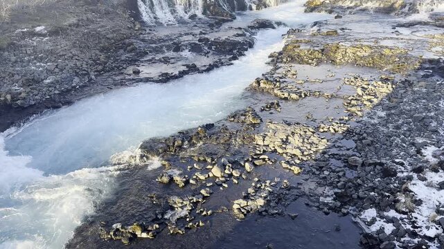 Handheld front view POV pan up shot of the thundering neon blue chasm at Bruarfoss waterfall Iceland
