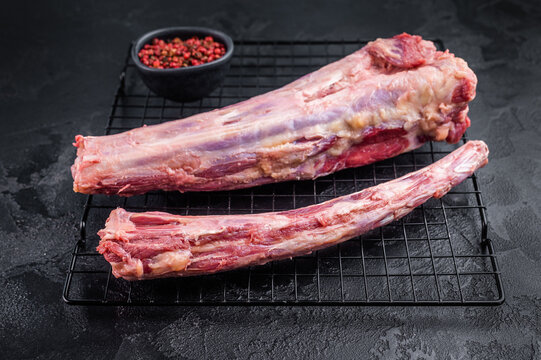 Raw beef oxtail segments on metal rack over dark textured background with copy space, butcher meat for broth and slow cooking