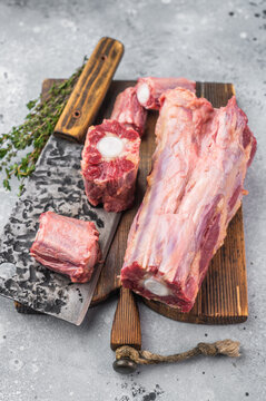 Raw beef oxtail pieces on wooden board with cleaver and thyme over light textured background with copy space