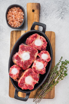 Raw beef oxtail pieces in cast iron skillet with thyme and rock salt, top view butcher style preparation for slow cooking