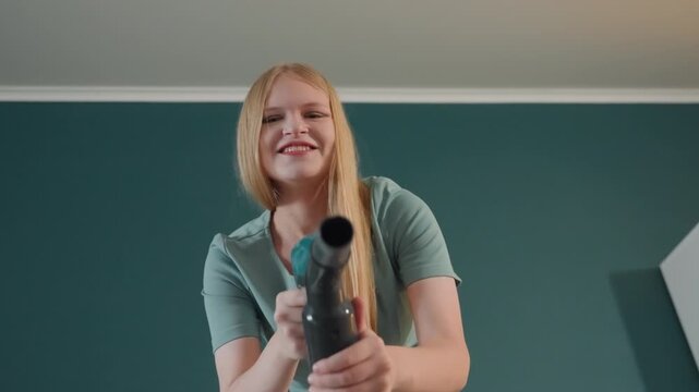 White woman playful vacuuming house, smiling homeowner dancing with hose, cordless nozzle gleaming, warm teal interior, lowangle joyful shots, lifestyle vibe, frames portray homeowner, entertainer,