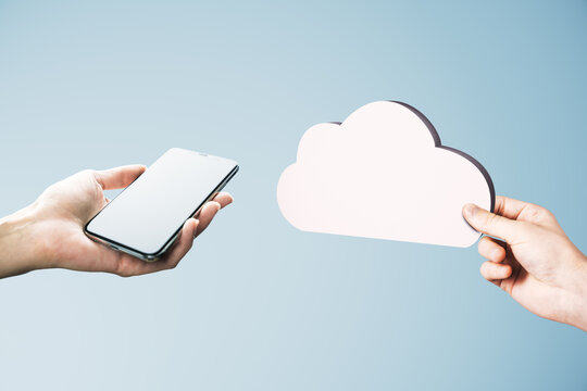 Hands holding a smartphone and paper cloud on a bright blue background, symbolizing digital connection, cloud storage, communication, and technology.