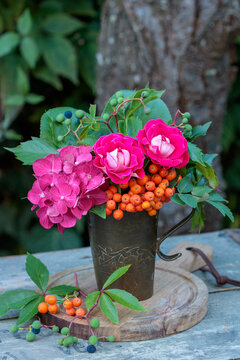 Blumenstrau&szlig; mit roten Rosen, Hortensienbl&uuml;ten, Ebereschen-Beeren und Wildem Wein im vintage Kupferbecher im Sommergarten