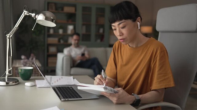 Asian woman e-learning and writing notes in home office