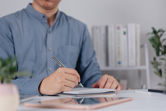 Businessman writing on notebook at desk with digital tablet for business planning