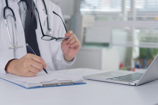 Doctor hands holding eyeglasses and writing medical report on clipboard