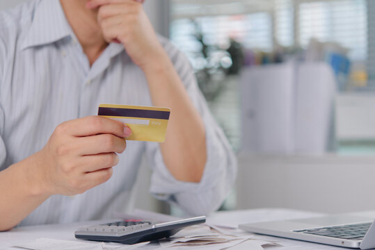 Man holding credit card and thinking about debt with calculator and receipts on desk