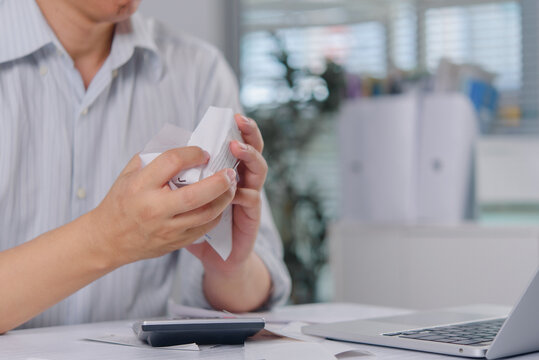 Stressed man crumpling paper receipts and bills at desk with calculator