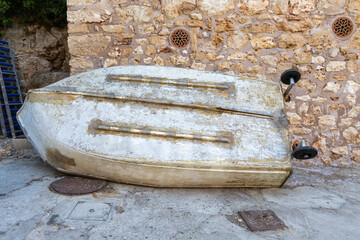 Weathered white dinghy resting against a stone wall © Michael