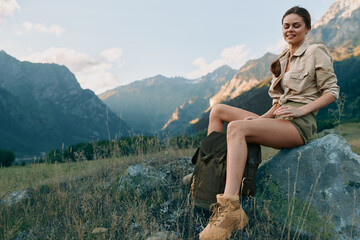 Obraz premium A woman outdoor in hiking attire sits on a rock above rugged mountains, presenting a relaxed, stylish lifestyle moment in nature and stunning landscape.