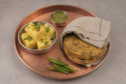 Copper tray with steamed dhokla and wrapped thepla, Indian snack preparation concept