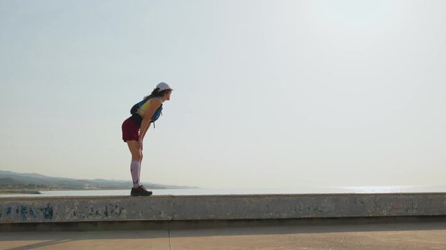 Runner stands on a concrete ledge. Calm focus guides her gaze. City and sea meet on the horizon. Her athletic wear suggests steady motion. Mid-stride, her feet strike the pavement