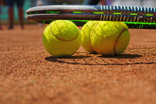  A yellow tennis ball and tennis racket lies on the clay court.