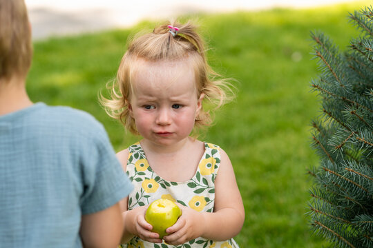 Serious Toddler Girl Holding Bitten Green Apple Outdoors