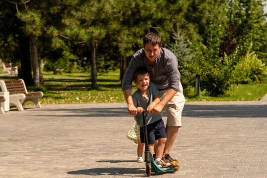 Smiling Boy Riding Scooter With Father in Park