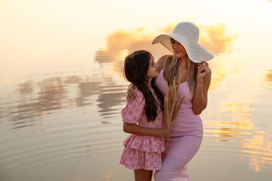 Mother And Daughter Exchanging Look Beside Sunset Lake
