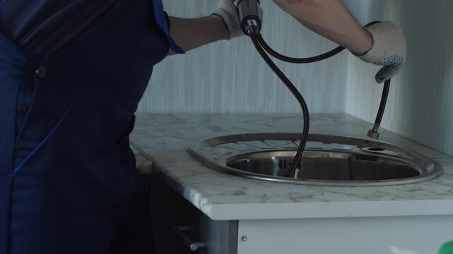 Plumber threads flexible hoses through the mounting hole and installs a faucet onto the kitchen sink. Experienced worker in protective gloves secures the tap onto the marble countertop