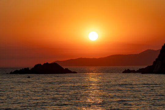 A serene sunset over the rocky seashore with vibrant orange and red hues, Budva, Montenegro