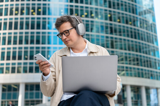Businessman Working on Laptop and Smartphone Outdoors Near Moder