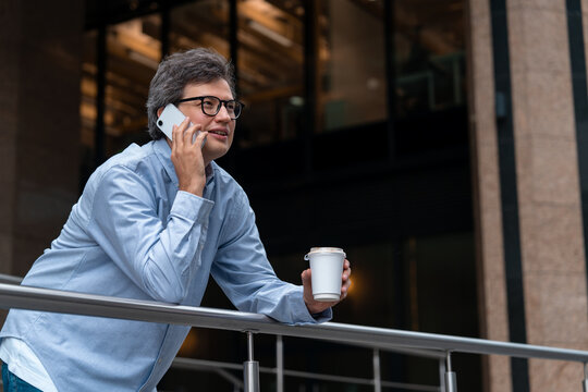 Businessman talking on smartphone while holding coffee outdoors,